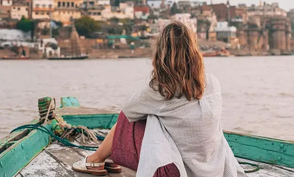 Traveler enjoying an evening boat ride on the Ganges River in Varanasi with city view in background.