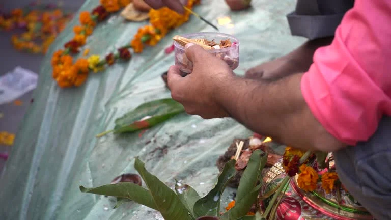 A man performing a Hindu ritual with sacred items and flowers on the banks of the Ganges, as part of the asthi visarjan ceremony in Varanasi