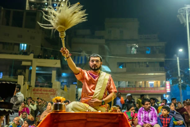 Priest performing Pind Daan in Kashi at a ghat during evening ritual with devotees in the background.