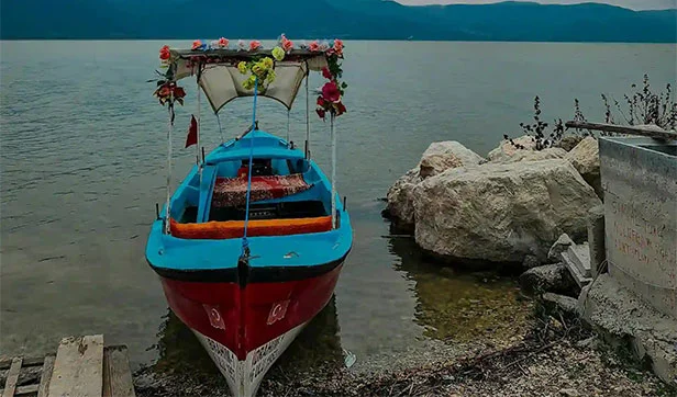 Decorated bajra boat with flowers on a calm lake with mountains in the background under cloudy sky.
