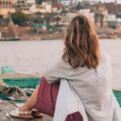 Traveler enjoying an evening bajra boat ride on the Ganges River in Varanasi with city view in background.