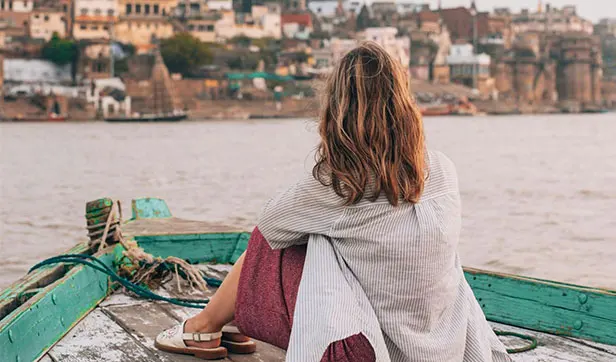 Traveler enjoying an evening bajra boat ride on the Ganges River in Varanasi with city view in background.